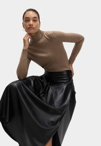 Brązowy sweter w serek z miękkiego materiału, połączony z zwiewną czarną skórzaną spódnicą midi, z wysokim stanem i subtelnym połyskiem.
