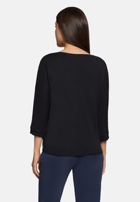 Zwarte top met lange mouwen, losse pasvorm, zachte textuur en opgerolde manchetten, voorzien van een ronde halslijn en een naad in het midden van de rug.