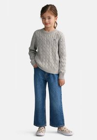 Maglione grigio a trecce, jeans blu larghi a gamba dritta e scarpe chiare con puntini neri. Design semplice, texture morbida e vestibilità casual.