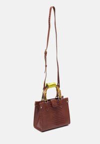 Sac à main en cuir marron à motif crocodile, avec une forme structurée, une anse supérieure jaune et une bandoulière réglable marron.