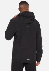 Schwarze wasserdichte Jacke mit Kapuze, mit strukturierter Oberfläche, weißem Akzent am Saum und kleinem blauem Logo auf der Rückseite.
