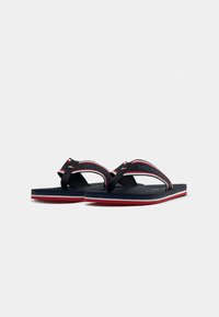 Black flip-flops with a textured sole, featuring a red and white striped accent on the straps labeled "HILFIGER." Smooth, lightweight design.
