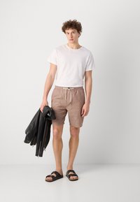Shorts légers dans une teinte marron atténuée avec une taille à cordon, associés à un t-shirt blanc uni et une veste en cuir noire. Sandales noires aux pieds.
