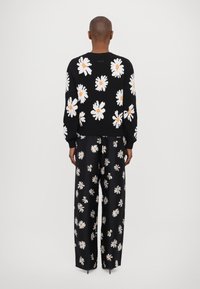 Svart stickad tröja med vita prästkragemönster och gula mittpunkter, kombinerad med svarta byxor med ett helmönstrat prästkragemönster.