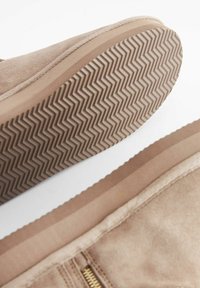 Beige suede ankle boot displaying a synthetic rubber sole with zigzag texture, side zipper detail, and smooth upper edge.