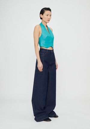 Geteiltes türkisfarbenes Leder-Haltertop, kombiniert mit hoch taillierten, dunkelblauen, weit geschnittenen Jeanshosen. Glatte Textur, klare Linien und minimalistische Details.