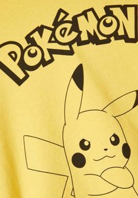 Maglietta gialla con una grafica di Pikachu in contorno nero, con il testo "Pokémon" sopra in lettere grasse nere, tessuto strutturato.