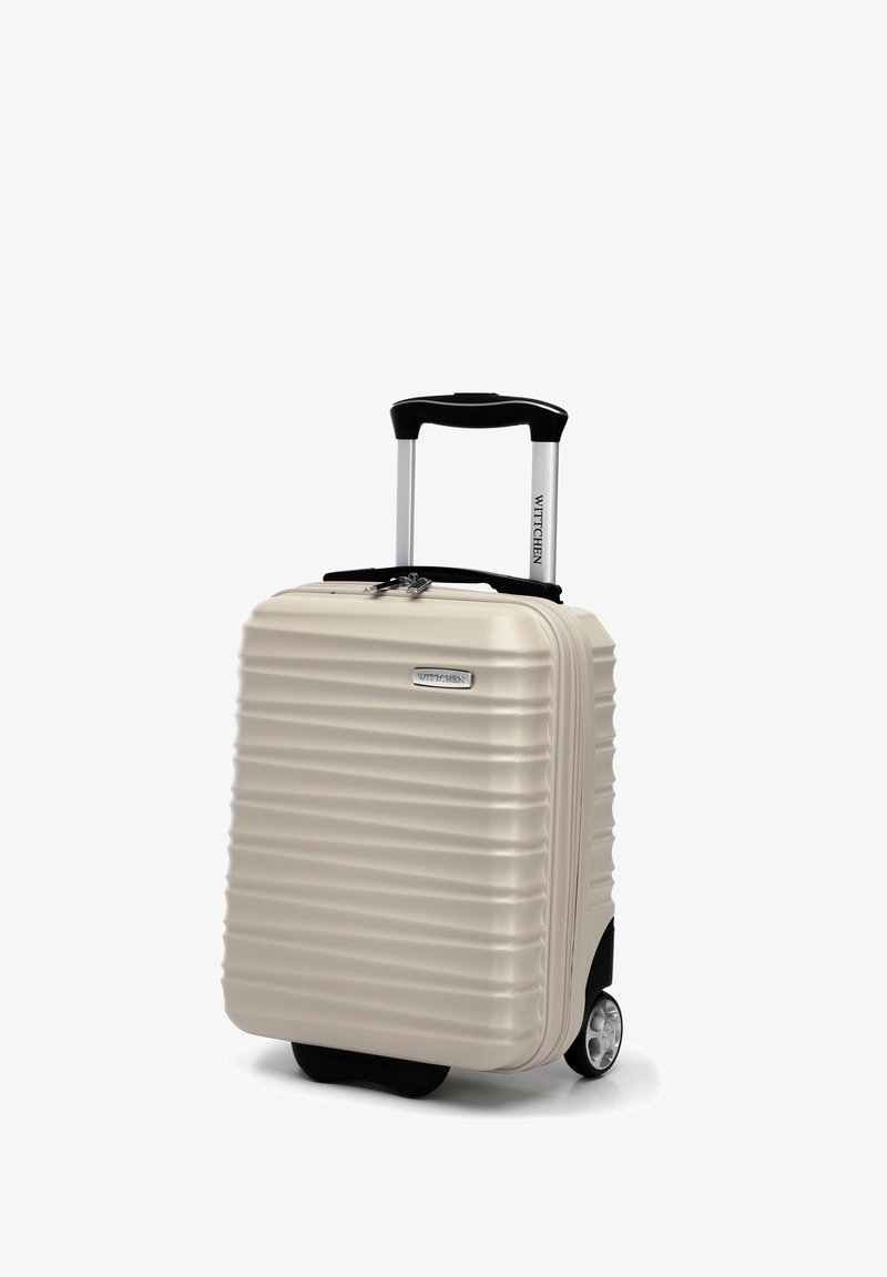 Valise rigide beige avec des rainures verticales, poignée rétractable et doubles roulettes. Présente un logo de marque argenté à l'avant.