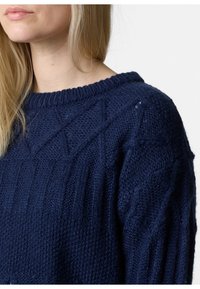 Dunkelblauer Strickpullover mit einem strukturierten Design, das am Vorderteil über gerippte und rautenförmige Muster verfügt, sowie einem runden Ausschnitt.