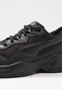 Sneakers neri con una parte superiore texturizzata che presenta materiali in mesh e sintetici. Punta arrotondata, lacci piatti e accenti del logo discreti.