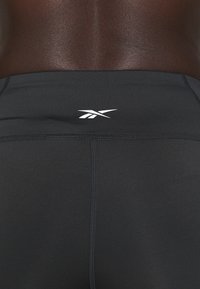 Black athletic shorts made of stretchy fabric with a snug fit. Features a small white logo on the back and flatlock seams for comfort.