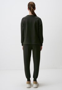Donkergroen sweatshirt en bijpassende joggers van zachte stof, met een ontspannen pasvorm, geribde boorden en witte sneakers.