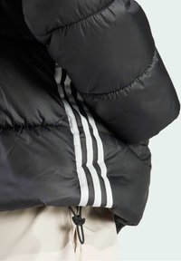 Svart puffjacka med en glänsande, quiltad yta, med tre vertikala vita ränder längs sidan och en justerbar dragsko i nederkant.