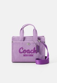 Purple denim tote bag with short handles, featuring "Coach New York" embroidered in bold lettering and an adjustable shoulder strap.
