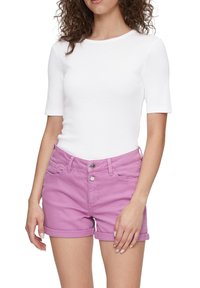 Witte kortekleurige top gecombineerd met roze denim shorts. De shorts hebben een knoopsluiting, opgerolde boorden en voorzakken.