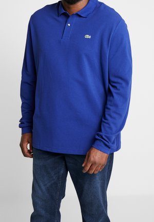 Polo bleu à manches longues en coton, avec un col classique, une patte de boutonnage et le logo vert Lacoste sur la poitrine.