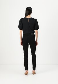 Black puff-sleeve top with a keyhole back detail, paired with fitted black jeans and beige strappy heels. Smooth texture, modern design.