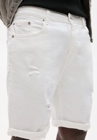 Șorturi din denim alb cu pete distruse. Prezintă un tiv răsucit și nasturi metalici la talie și buzunare. Textură netedă.