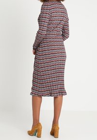 Robe plissée multicolore présentant un motif à rayures ondulées dans des tons de bleu, rouge et crème. Manches longues, longueur genou, et taille élastique.