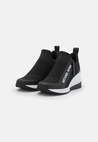 Sorte strikkede joggesko med en teksturert mesh-overdel, hvite logo detaljer og en kontrasterende hvit såle. Har et slip-on design med hæltrekk.