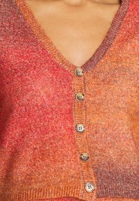 Cardigã tricotado com decote em V, tonalidades em degradê de vermelho e laranja, e seis botões com acabamento texturizado ao longo da aba.