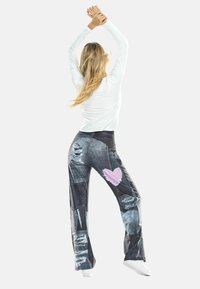 Jeans mit Schlag und ausgewaschenen Details, versehen mit einem pinkfarbenen Herzpatch. Kombiniert mit einem weißen Langarmshirt und weißen Schuhen.