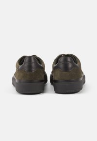 Green suede sneakers with black leather accents, rubber soles, and padded heel tabs, featuring a minimalistic design and lace-up closure.