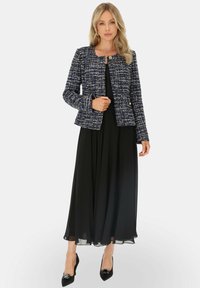 Granatowa i biała tweedowa kurtka z okrągłym dekoltem i złotym zapięciem, w połączeniu z zwiewną czarną sukienką i spiczastymi czarnymi szpilkami.
