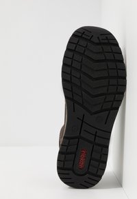 Schwarze Gummisohle mit einem strukturierten Muster für besseren Halt, gekennzeichnet durch ein semi-sichtbares braunes Schuhoberteil und einem roten "rieker"-Logodetail.