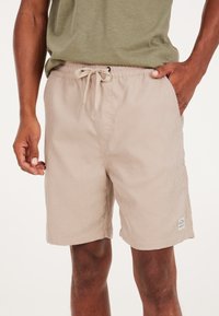Pantaloni corti in cotone a costine beige con un motivo testurizzato, una vita elasticizzata e un cordoncino. Presentano tasche laterali e una patch con il marchio sull'orlo.