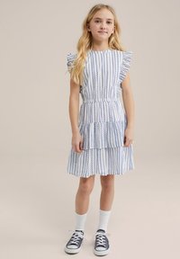 Rochie albă cu dungi verticale albastre, manșete volan, talie strânsă și fustă în straturi. Purtați cu adidași bleumarin și șosete albe.