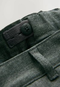 Sivá textilná páska s čiernym gombíkom s dizajnom kvetu a vyrazeným textom "Clarks". Zahrnuje textilný slučku pre nastaviteľnosť.