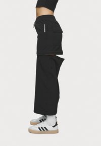 Svarte cargo shorts med en avslappet passform, glidelås ved bunnen og side lommer, laget av lett materiale. Kombinert med hvite og svarte sneakers.