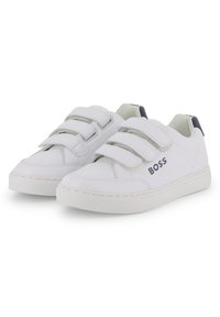 Witte sneakers met drie klittenbandsluitingen, een gestructureerde zool en een marineblauwe accent op de hiel. "BOSS" logo in marineblauw op de zijkant.