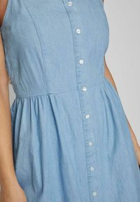 Ljusblå denimklänning med knäppning fram, ärmlös design, insamlad midja och slät textur.