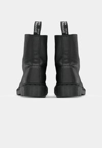 Botas de tobillo de cuero negro vistas desde atrás, con suelas gruesas y tiradores que dicen "CON SUELAS REBOTANTES".