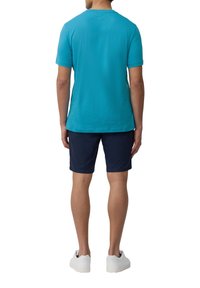 Turquoise katoenen T-shirt met korte mouwen, gecombineerd met marineblauwe shorts. Model draagt witte sneakers, gezien van achteren. Eenvoudig ontwerp, geen patronen.