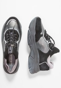 Mustat ja hopeaiset lenkkarit, joissa on tekstuurilla viimeistelty metalliset yksityiskohdat, mokkanahkaa ja verkkomateriaaleja, pyöreä kärki, paksu pohja ja mustat nauhat.