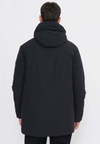 Schwarze Steppjacke mit hohem Kragen und Kapuze. Glatte Textur, verlängertes Design und Seitentaschen. Verfügt über einen dezenten Glanz.