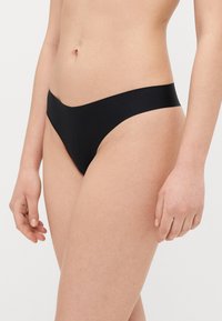 Black thong underwear made of smooth, stretchy fabric. Features a minimal design with a low-rise waistband and no visible seams.