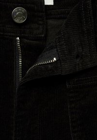 Black corduroy fabric with a visible zipper and button closure. Includes a stitched inner lining and fine vertical ribbing texture.