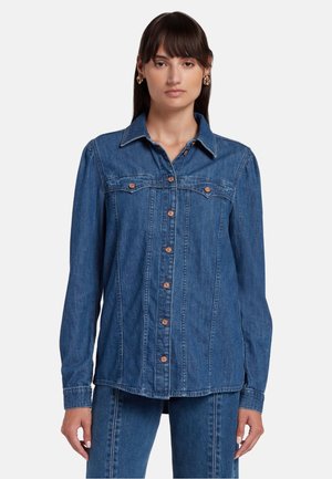 Blauwe denim shirt met kraag, sluiting met knopen aan de voorkant en twee borstzakken. Heeft lange mouwen en een rechte snit met zichtbare naaddetails.