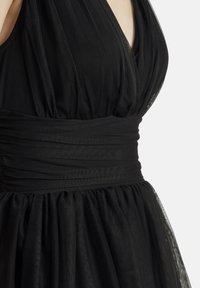 Robe noire avec un décolleté en V profond, tissu en tulle froncé et taille large ; texture douce avec des sections de jupe superposées et fluides.