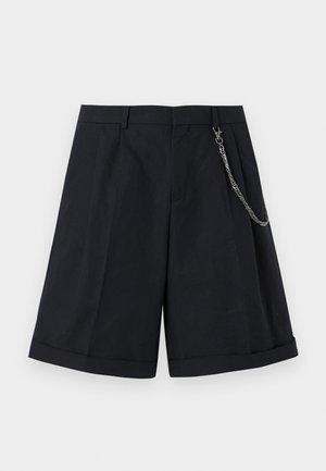 Μαύρα, ραμμένα μέχρι το γόνατο σορτς με πτυχώσεις μπροστά, μανσέτες στα τελειώματα, θηλιές για ζώνη και ασημένια αλυσίδα δεμένη στη δεξιά πλευρά.