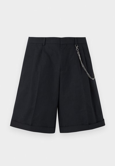 Μαύρα, ραμμένα μέχρι το γόνατο σορτς με πτυχώσεις μπροστά, μανσέτες στα τελειώματα, θηλιές για ζώνη και ασημένια αλυσίδα δεμένη στη δεξιά πλευρά.