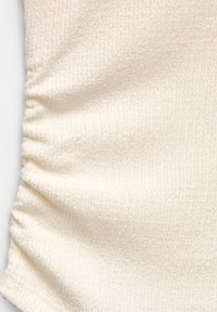 Tessuto color crema chiaro con una superficie testurizzata, caratterizzato da dettagli arricciati su un lato. Materiale morbido e leggermente elasticizzato.