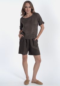 Bruine linnenoutfit met een loszittend top met opgerolde mouwen en bijpassende shorts met een elastische tailleband, gecombineerd met geweven instapschoenen.