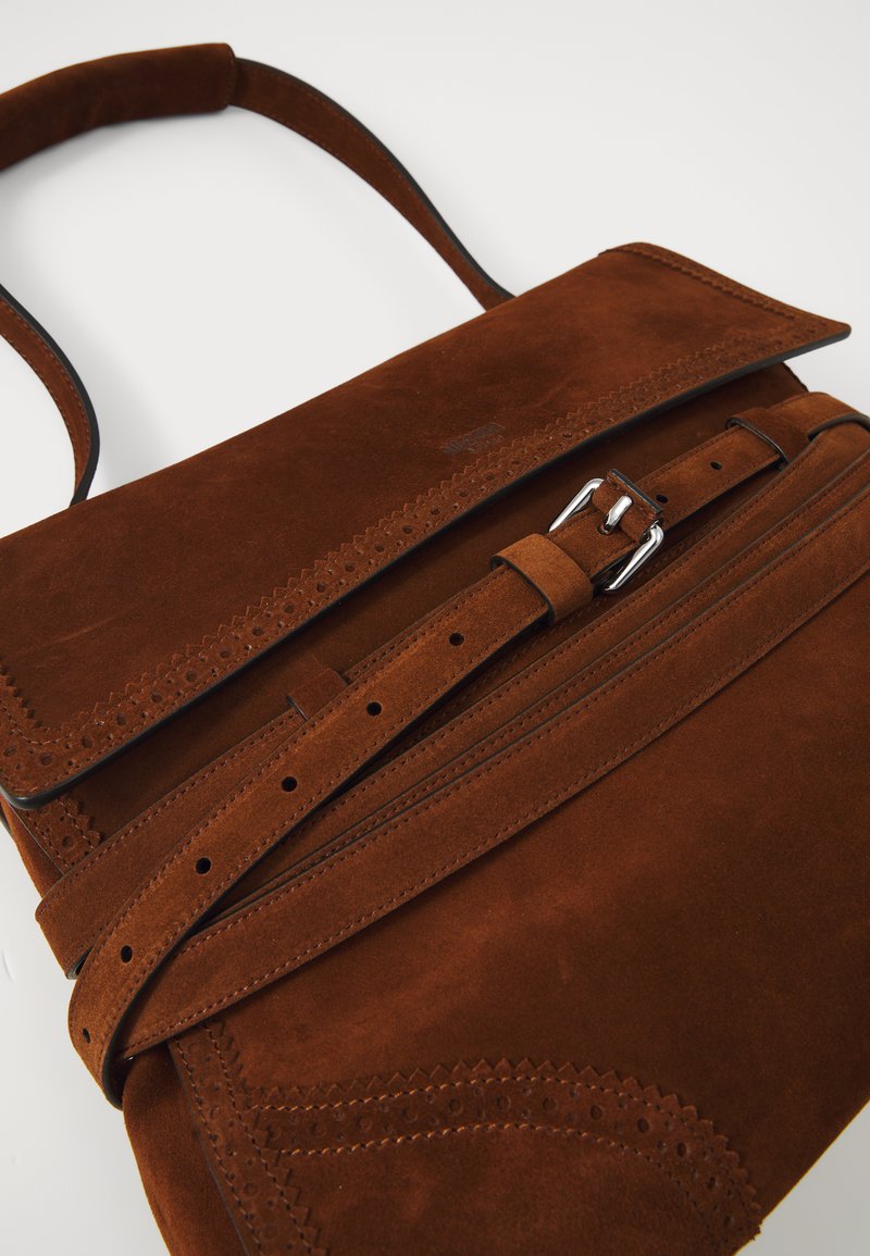 Brun mockaskinnsväska med en strukturerad design, som har ett lock, spänne för stängning och perforerade accenter längs kanterna.