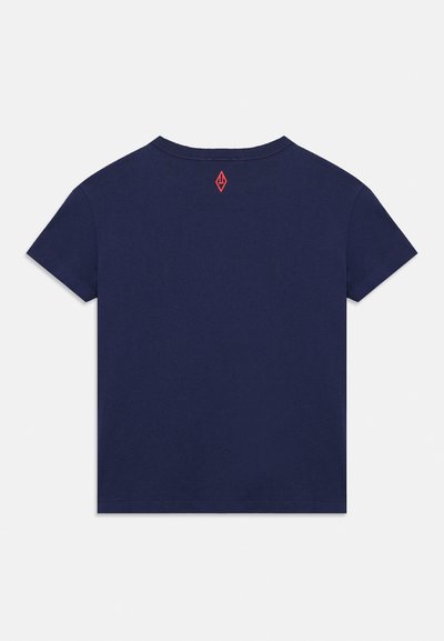 Μπλε ναυτικό κοντομάνικο T-shirt, φαίνεται από πίσω, με ένα μικρό κόκκινο γεωμετρικό λογότυπο κάτω από τον λαιμό.