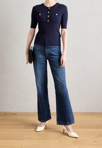 Granatowy prążkowany sweter z krótkimi rękawami i złotymi guzikami, zestawiony z rozkloszowanymi niebieskimi dżinsami i beżowymi szpilkami z wąskim noskiem.